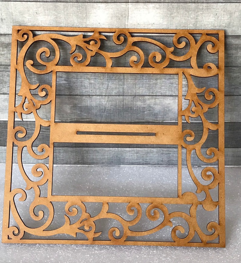 Puede incluir: Un marco de madera con un dise&ntilde;o decorativo e intrincado. El marco tiene un recorte en el centro, creando un espacio para una imagen u otro elemento decorativo.