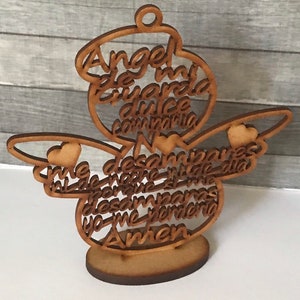 May include: A wooden angel-shaped decoration with the Spanish text "Angel de mi guarda, dulce compañía". The angel has outstretched wings with heart accents and stands on a circular base. The wood has a natural, light brown color.