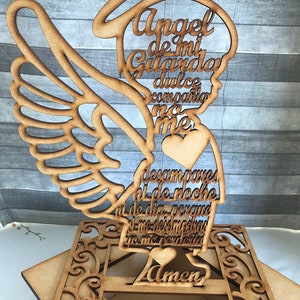 Puede incluir: Un recorte de madera de un &aacute;ngel con alas, un halo y un coraz&oacute;n. El &aacute;ngel sostiene un rollo con el texto "Angel de mi Guarda dulce compania no me desampares ni de noche ni de dia porque si me desmayara tu me perdones Amen".