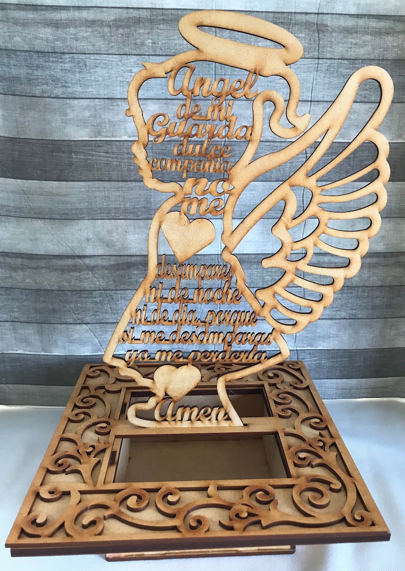May include: Wooden angel-shaped decorative piece with an openwork design. The angel has a halo, wings, and holds a heart. Text in Spanish is cut into the wood. The base has an ornate, openwork design.