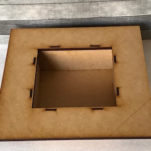 Puede incluir: Una caja de madera con una abertura cuadrada. La caja est&aacute; hecha de madera marr&oacute;n claro y tiene un acabado liso. La abertura est&aacute; rodeada por un marco delgado de color marr&oacute;n oscuro.