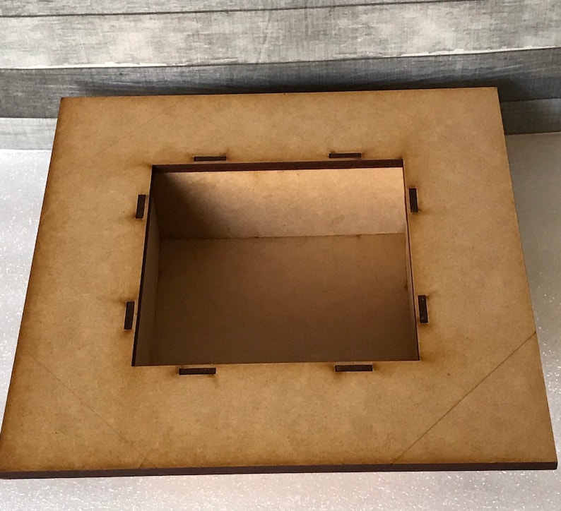 Puede incluir: Una caja de madera con una abertura cuadrada. La caja est&aacute; hecha de madera marr&oacute;n claro y tiene un acabado liso. La abertura est&aacute; rodeada por un marco delgado de color marr&oacute;n oscuro.