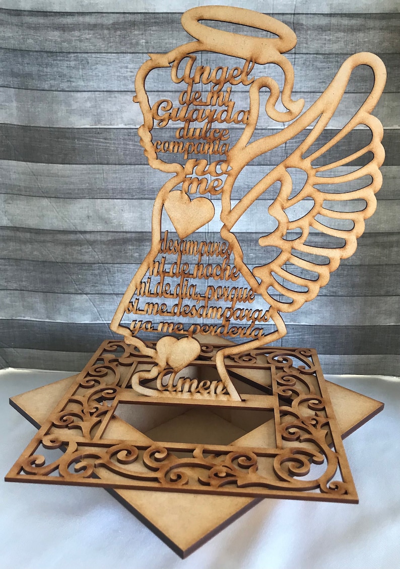 May include: A wooden angel-shaped decoration with an openwork design. The angel has wings, a halo, and text in Spanish. The base is a decorative square with an open center and ornate cutouts. The overall color is light brown.