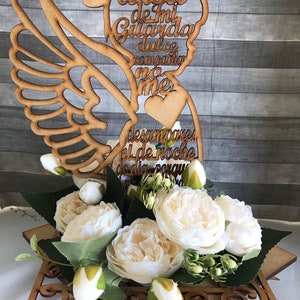 Puede incluir: Figurita de &aacute;ngel de madera con alas, un coraz&oacute;n y el texto "Angel de mi Guarda dulce compania no me desampares ni de noche ni de dia". La figurita est&aacute; colocada en una base de madera con un dise&ntilde;o decorativo y rodeada de flores blancas.