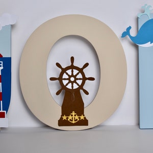 Puede incluir: Letras de madera que deletrean "JOH" en azul, beige y azul claro. La "J" tiene un faro rojo y blanco, la "O" tiene un tim&oacute;n de barco marr&oacute;n con un ancla dorada, y la "H" tiene una ballena azul con vientre blanco.