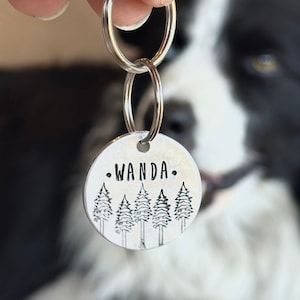 以下が含まれることがあります： 銀製の犬用タグに「WANDA」という名前が刻印されており、小さな松の木の列で囲まれています。タグは銀製のキーリングに取り付けられています。