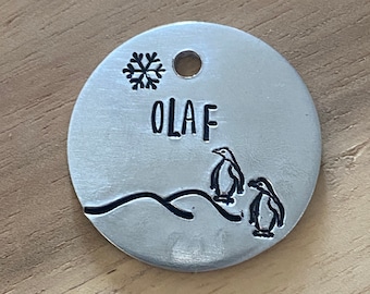 May include: Silver metal pet tag with a snowflake, two penguins, and the name "OLAF" engraved on it.