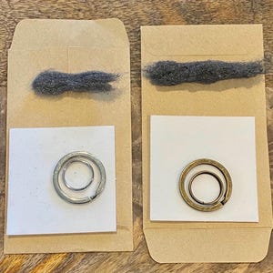 May include: Two small brown paper envelopes each containing a metal keyring and a bundle of gray steel wool. One keyring is silver, the other is brass-colored, both with a small inner ring.