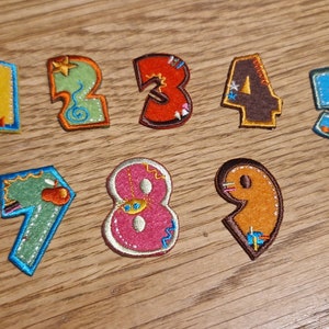 May include: Ten colourful felt patches shaped like numbers 1 through 10. Each number has a different design and colour, including yellow, green, red, brown, blue, white, and orange.