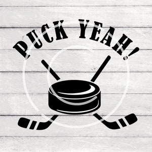 Può includere: Grafica in bianco e nero con il testo "Puck Yeah!" in grassetto. Due bastoni da hockey sono incrociati dietro un disco da hockey nero.