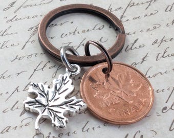 May include: A copper-colored keychain with a silver maple leaf charm and a Canadian penny dated 2012. The keychain ring is a dark bronze color, and the penny has a maple leaf design.
