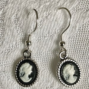 May include: A pair of silver earrings with a black and white cameo design. The cameo features a woman's profile in white against a black background.