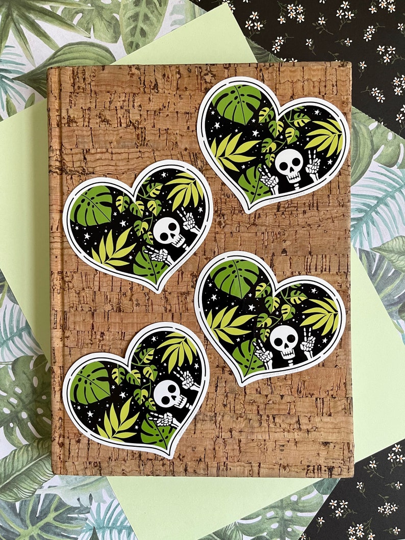 May include: Four heart-shaped stickers with a black background and green tropical leaves. Each sticker features a white skeleton with a skull wearing a peace sign.