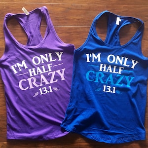 May include: Two racerback tank tops with the text "I'm only half crazy 13.1" printed on them. One tank top is purple and the other is blue.
