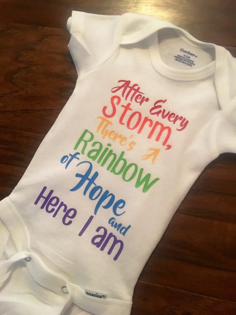 May include: White baby onesie with a rainbow-colored graphic that reads "After Every Storm, There's A Rainbow of Hope and Here I am".