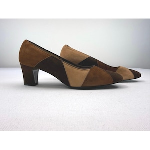 May include: A pair of brown suede heels with a geometric color block design. The shoes feature a medium heel and a pointed toe. The color palette includes shades of light brown, medium brown, and dark brown.