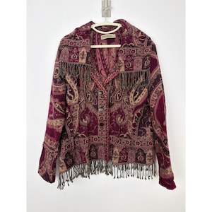 May include: A long-sleeve jacket in shades of deep burgundy and tan, featuring an intricate paisley pattern throughout. The garment includes a wide collar, a front button closure, and decorative fringe detailing along the hem and collar.