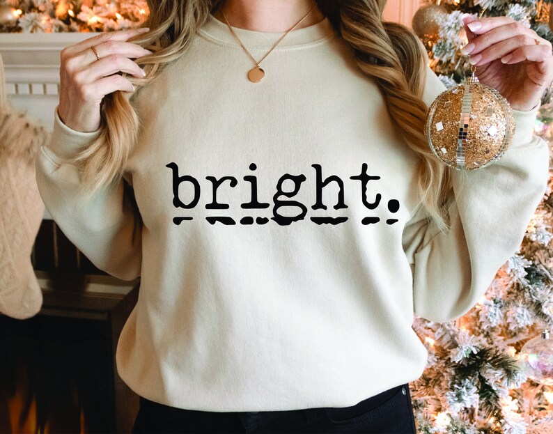 Puede incluir: Una sudadera de color crema con la palabra "bright" impresa en letras negras. Las letras tienen una fuente de m&aacute;quina de escribir vintage.