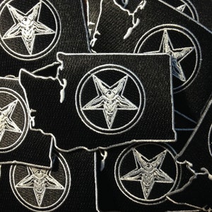 May include: A stack of black fabric patches with a white pentagram and goat head design in a circle. The patches are shaped like the state of Washington.