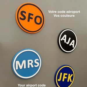 Peut inclure: Quatre autocollants ronds avec des codes d'aéroport. Les autocollants sont de couleurs différentes et ont un texte blanc. Les codes sont SFO, MRS, AJA et JFK.