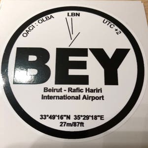 Peut inclure: Un autocollant circulaire blanc avec une bordure noire et le texte "BEY" en grandes lettres noires. Le texte "Aéroport international de Beyrouth - Rafic Hariri" est sous les lettres. Les coordonnées "33°49′16″N 35°29′18″E" et l'altitude "27m/87ft" sont sous le nom de l'aéroport. Le texte "OACI: OLBA", "LBN" et "UTC +2" sont autour du cercle.