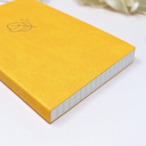 May include: A small, yellow notebook with a white spine and a simple leaf design on the cover.