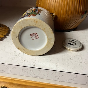 Può includere: Vaso in ceramica bianca con coperchio e un disegno dipinto di persone in abiti tradizionali. Il vaso ha un timbro con caratteri cinesi sul fondo.