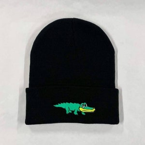Könnte beinhalten: Schwarze Mütze mit einem grünen Alligator, der auf der Vorderseite gestickt ist.