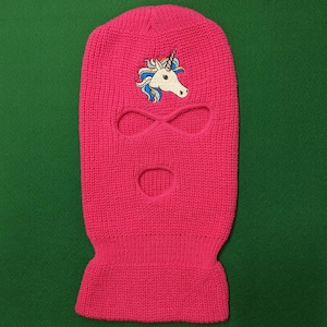 May include: Pink knitted ski mask with a white unicorn embroidered on the front.