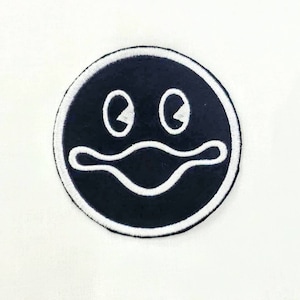 Puede incluir: Parche bordado en blanco y negro de una cara de dibujos animados con ojos grandes y una boca ancha.