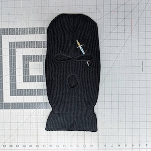 May include: Black knitted balaclava with a small embroidered silver knife design.