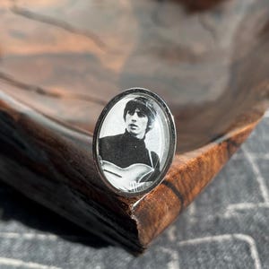 Könnte beinhalten: Ein silberner Ring mit einem Schwarzweißfoto eines Mannes, der Gitarre spielt. Das Foto ist in einer durchsichtigen Harzkuppel eingefasst.