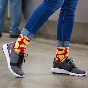 May include: A person wearing a pair of grey sneakers with white soles and colorful socks with a pattern of yellow and red. The socks feature a design of pastry-like shapes.