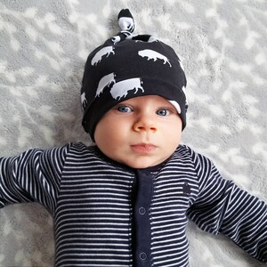 May include: A baby wearing a black and white striped onesie and a black knit hat with a white cow print. The hat has a knot on top.