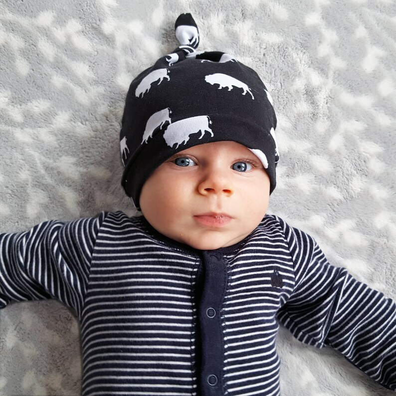 May include: A baby wearing a black and white striped onesie and a black knit hat with a white cow print. The hat has a knot on top.