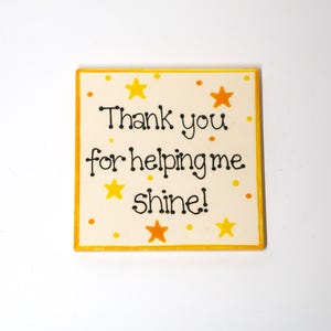Könnte beinhalten: Ein gelbes und oranges Holzschild mit dem Text "Danke, dass du mir hilfst zu strahlen!" und gelben Sternen auf weißem Hintergrund.