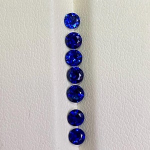 May include: A row of seven round, deep blue gemstones on a white surface.