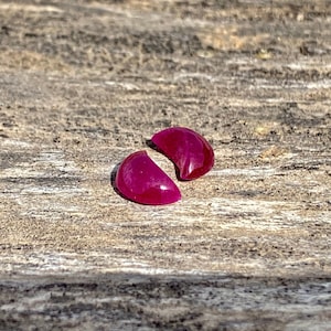 Puede incluir: Dos piedras preciosas rosadas en forma de media luna sobre una superficie de madera.