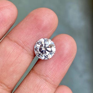 May include: A clear round gemstone with many facets, held in a hand.