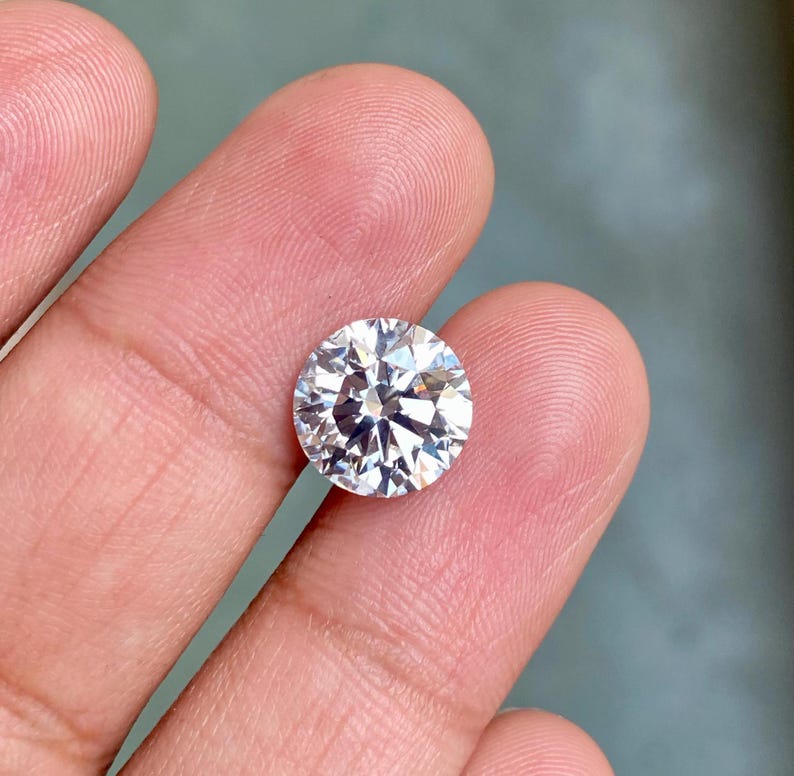 May include: A clear round gemstone with many facets, held in a hand.