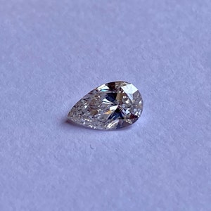 May include: A pear-shaped diamond gemstone with a clear, brilliant cut. The diamond is set against a white background.