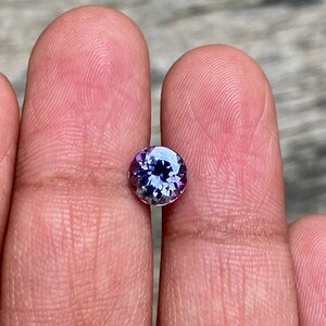 May include: A round, faceted gemstone with a purple and blue colour gradient. The gemstone is set in a clear bezel setting.