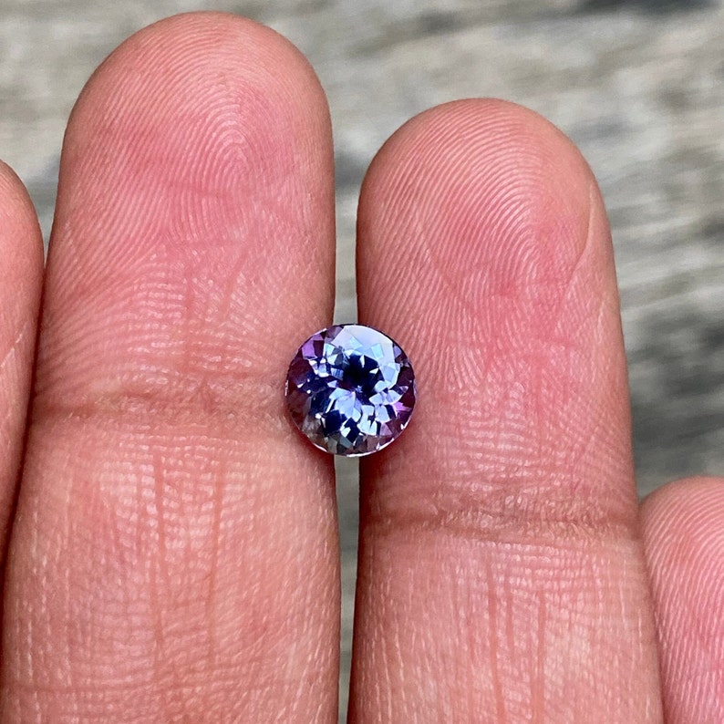May include: A round, faceted gemstone with a purple and blue colour gradient. The gemstone is set in a clear bezel setting.