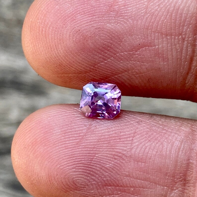 Puede incluir: Una piedra preciosa de forma cuadrada, de color p&uacute;rpura claro, con corte facetado.