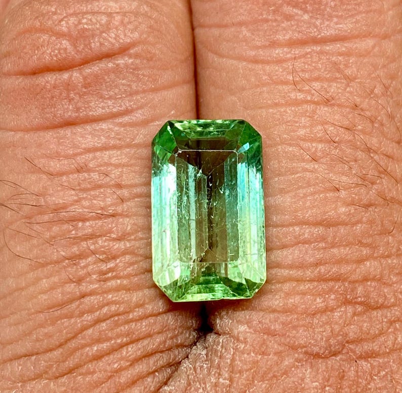 May include: A vibrant green emerald gemstone cut in an emerald shape.