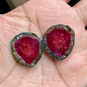 Pu&ograve; includere: Due cristalli di turmalina watermelon rosa e verde con una superficie liscia e lucida. I cristalli sono tagliati a met&agrave;, rivelando l'interno rosa.