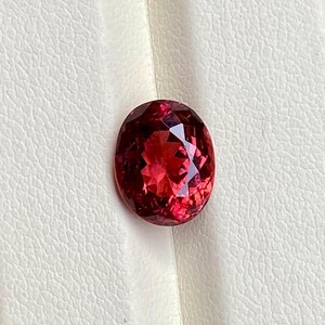 K&ouml;nnte beinhalten: Ein ovaler Edelstein in tiefroter Farbe mit Facetten.