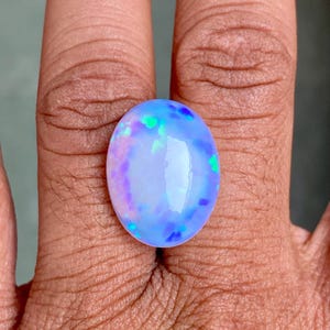 May include: A light blue oval opal gemstone with iridescent flashes of green, blue, and purple.