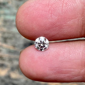 May include: A clear round diamond gemstone with facets, set in a ring setting.