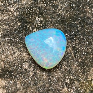 May include: A light blue iridescent opal gemstone with a teardrop shape. The opal has a white base with a blue and green iridescent sheen.